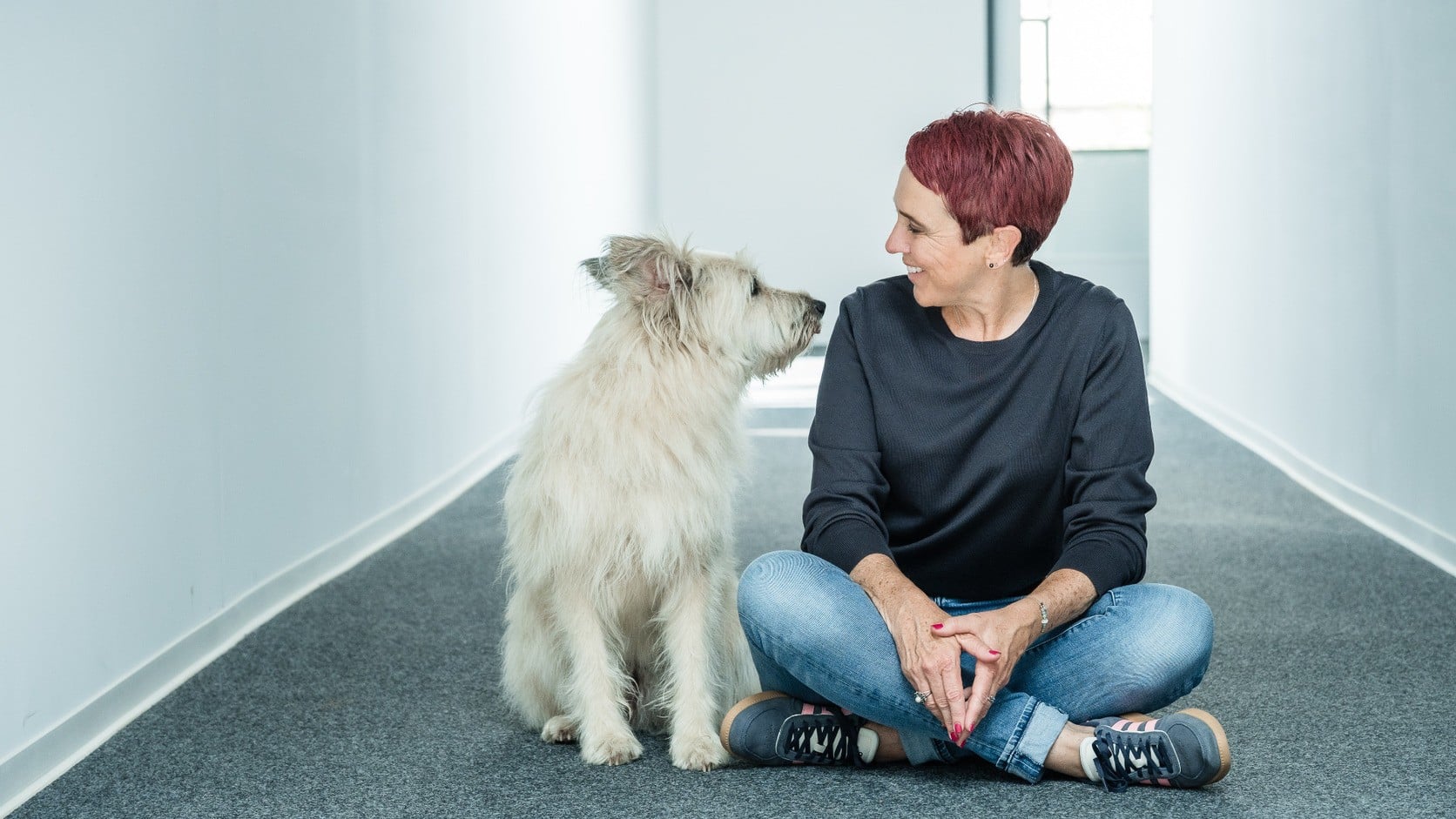 Nadine Pötz sitzt mit ihrem hellen Hund in einem Flur.