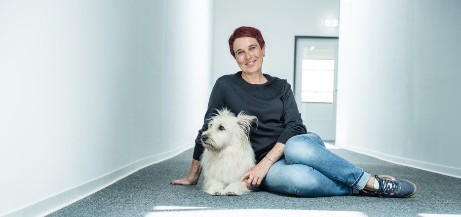 Nadine Pötz sitzt mit ihrem hellen Hund in einem Flur.